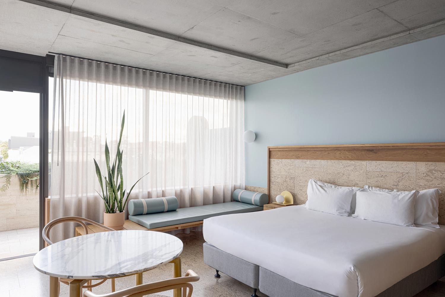 A Calile guest room with concrete ceiling, blue accent wall, and a curtained terrace.
