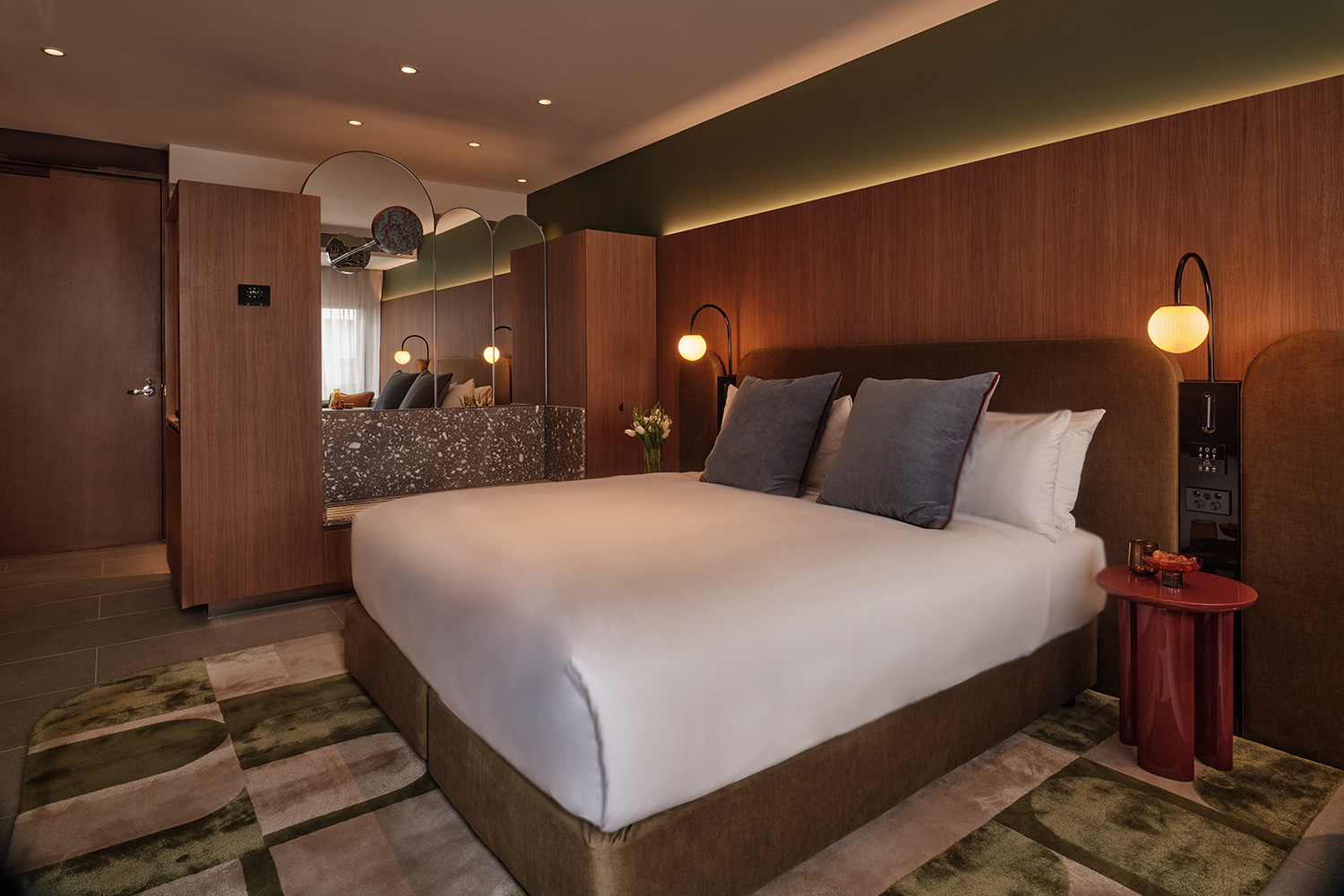 A bedroom at The Eve with walnut headboard wall, deep green ceiling detail, and a red bedside table.