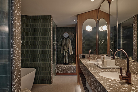 The Sunset Suite bathroom in deep green tile and terrazzo, with a freestanding bath.