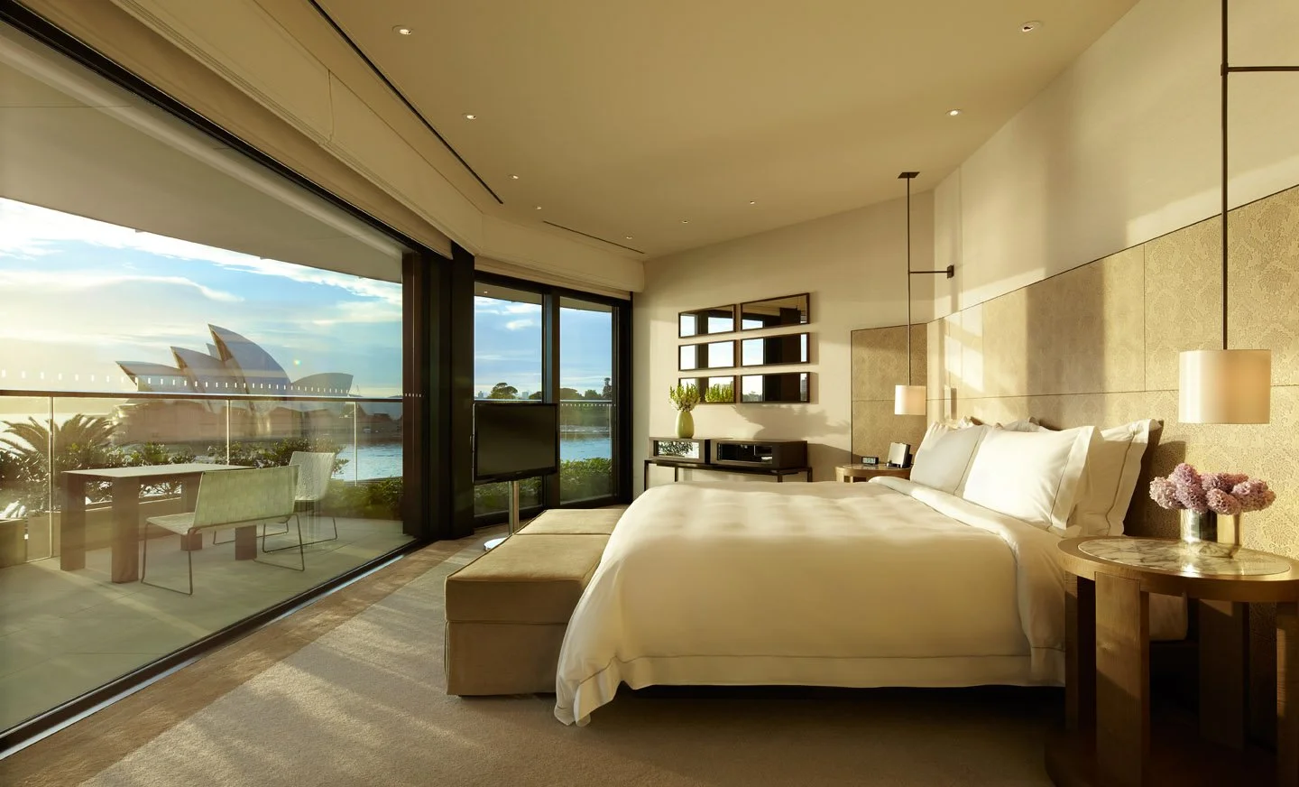 The master bedroom of the Sydney Suite at dawn, the Opera House visible through the window.